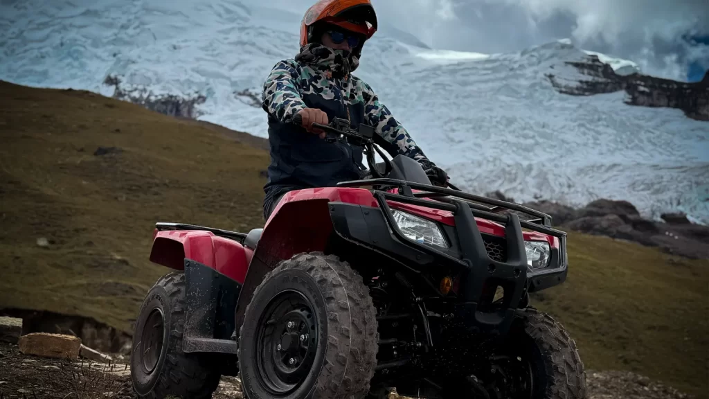 Persona conduciendo una cuatrimoto roja en una ruta de aventura cerca de la Montaña Ausangate, en Cusco, Perú, con un paisaje de nieve y montaña al fondo, Ausangate Cusco