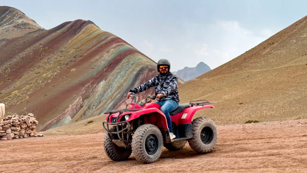 Turista conduciendo una cuatrimoto roja frente a la Montaña de 7 Colores durante el tour de aventura.