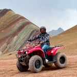 Turista conduciendo una cuatrimoto roja frente a la Montaña de 7 Colores durante el tour de aventura.