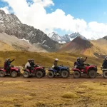Grupo de turistas en cuatrimotos recorriendo los Andes hacia la Montaña de 7 Colores, con montañas nevadas al fondo.