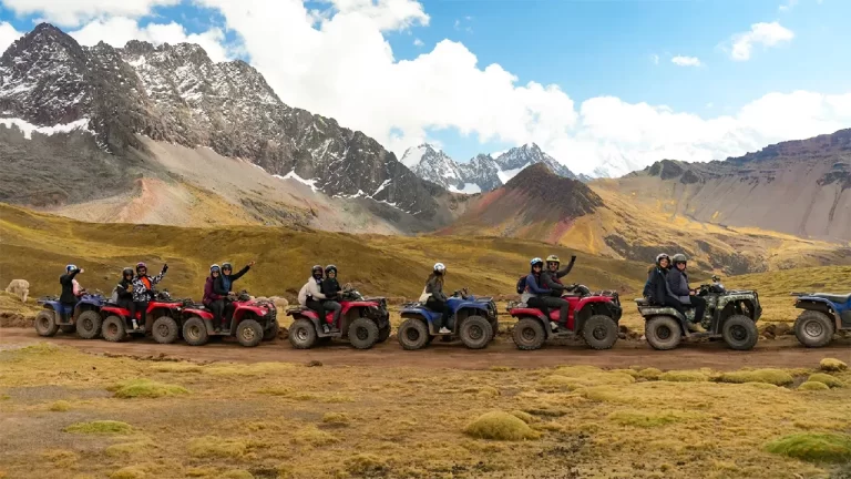 Grupo de turistas en cuatrimotos recorriendo los Andes hacia la Montaña de 7 Colores, con montañas nevadas al fondo.