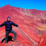 Turista posando en el mirador del Valle Rojo en Cusco, con paisajes intensos y montañas rojizas alrededor.