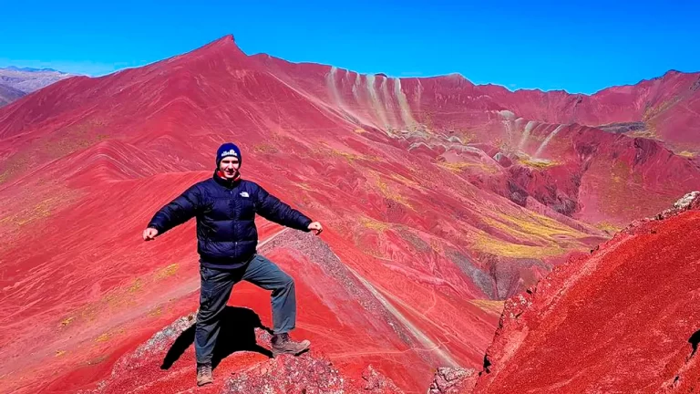 Turista posando en el mirador del Valle Rojo en Cusco, con paisajes intensos y montañas rojizas alrededor.
