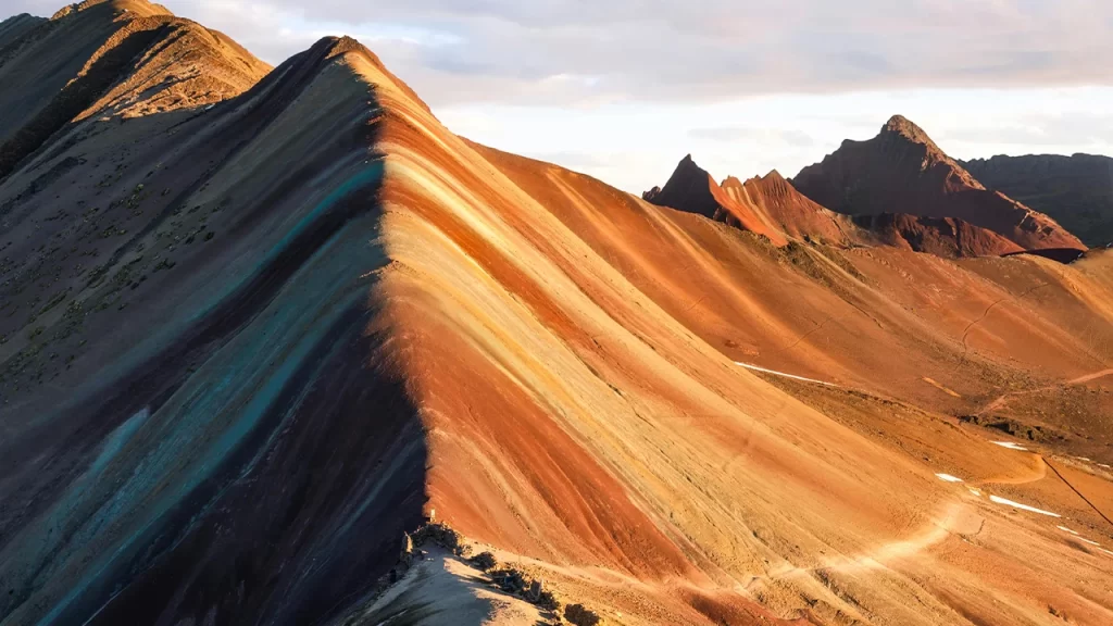 Vista panorámica de la Montaña de 7 Colores iluminada por el sol, mostrando sus franjas naturales multicolores.