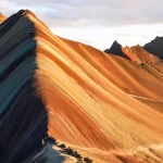 Vista panorámica de la Montaña de 7 Colores iluminada por el sol, mostrando sus franjas naturales multicolores.